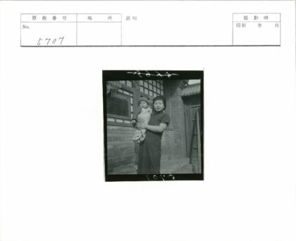 妇女抱婴儿站砖房外.jpg