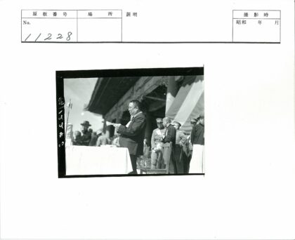 军人平民聚集木建筑前读报场景.jpg