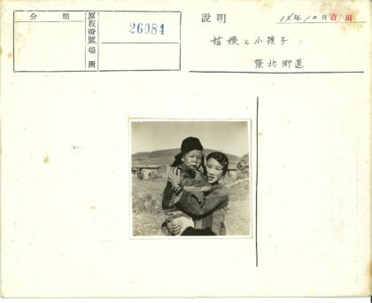 女孩抱孩子在山区小屋前.jpg