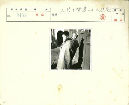 孩童背娃娃站木门建筑旁.jpg