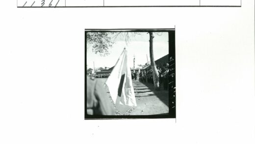 队伍举旗沿泥路前行背景建筑树木.jpg